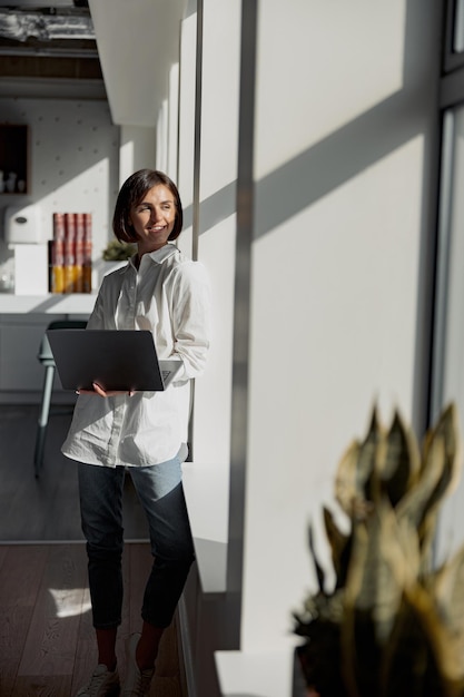 Photo european business woman in casual clothe with laptop standing in modern office and looking away