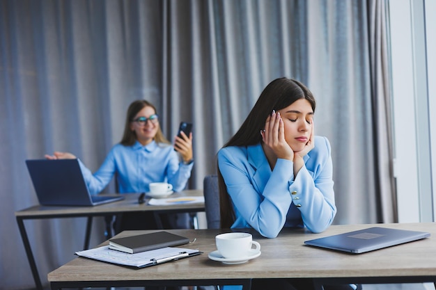 A European businesswoman is talking on a mobile phone while her European colleague is working in the background Concept of modern successful women Young girls sitting at desks in sunny office