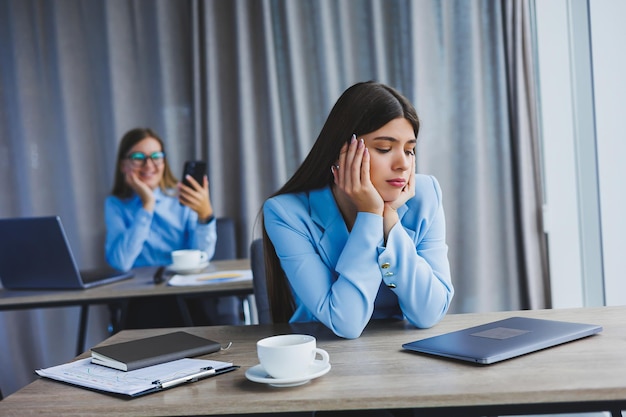 A European businesswoman is talking on a mobile phone while her European colleague is working in the background Concept of modern successful women Young girls sitting at desks in sunny office