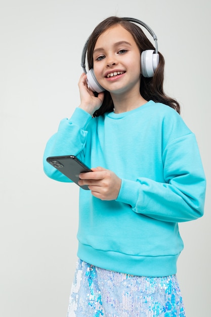 European cute young girl in a blue blouse relaxes with music in large stylish headphones with a phone in her hands on an studio