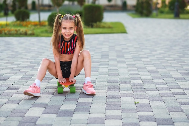 european girl of school age in short black shorts and a pink top riding a skateboard at summer park