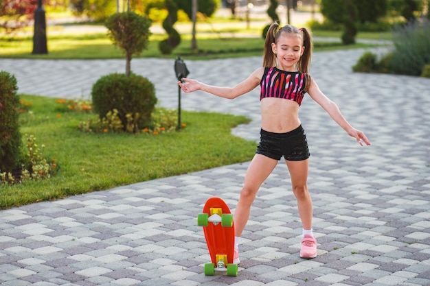 european girl of school age in short black shorts and a pink top riding a skateboard at summer park