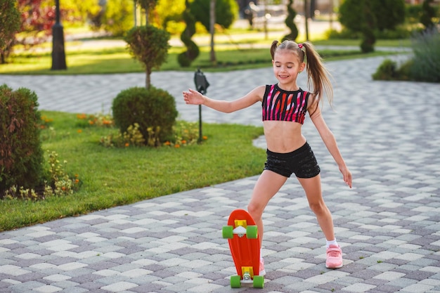 european girl of school age in short black shorts and a pink top riding a skateboard at summer park