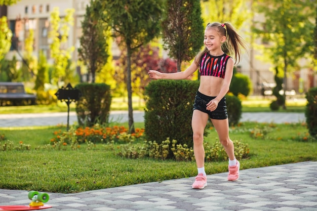 european girl of school age in short black shorts and a pink top riding a skateboard at summer park