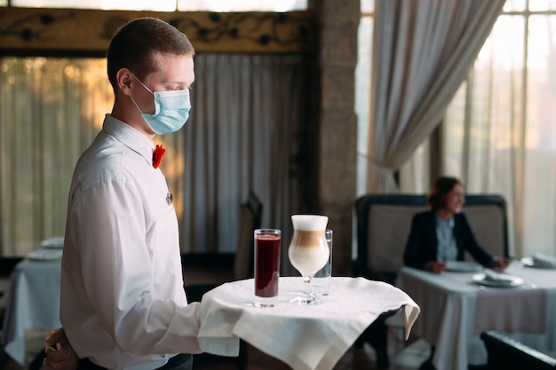 A European-looking waiter in a medical mask serves Latte coffee.