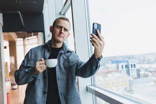 European male freelancer in checking notification on smartphone about money transactions doing business online working remotely while in cafe and drinking coffee