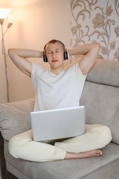 A European man with his eyes closed throws his hands behind his headsits on the sofa in headphones and listens to music