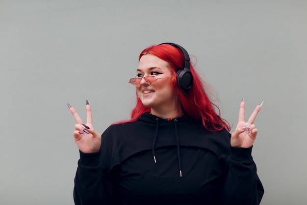 European plus size woman in headphones showing v victory fingers sign young red pink haired body pos...