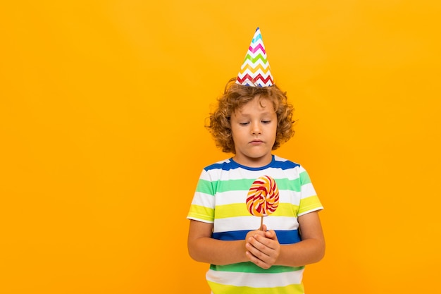 European red-haired curly-haired boy in a striped T-shirt with candy isolated over yellow 