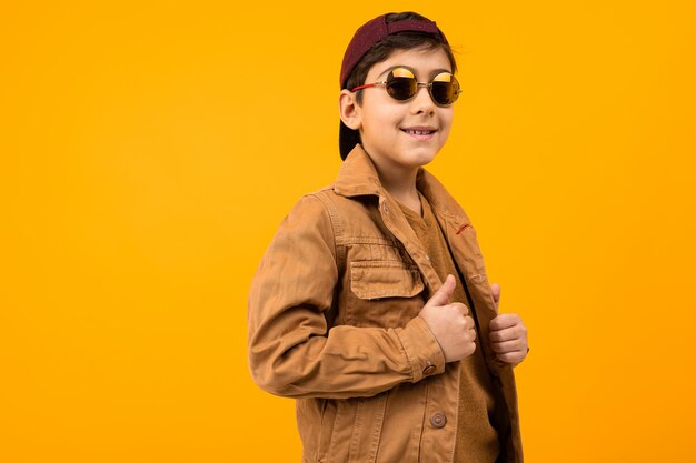 Photo european stylish teenager boy in a brown denim jacket and stylish glasses posing on a yellow background with copy space