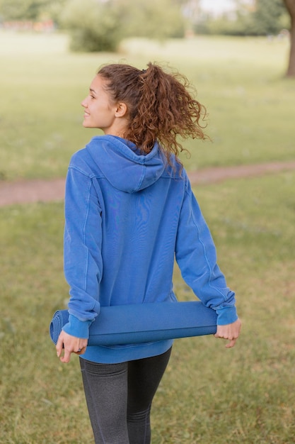 A european woman in a blue hoodie with a blue yoga mat chooses a place to do sports and meditation