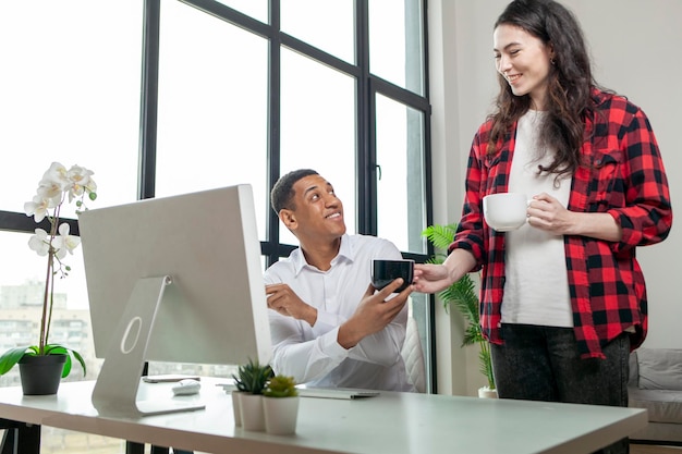 european woman brought tea to her husband african american who works and sits at computer