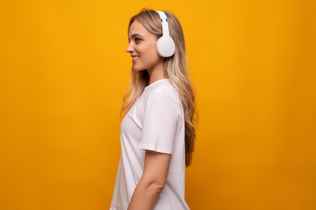 European woman closeup with big headphones on a yellow background with empty space