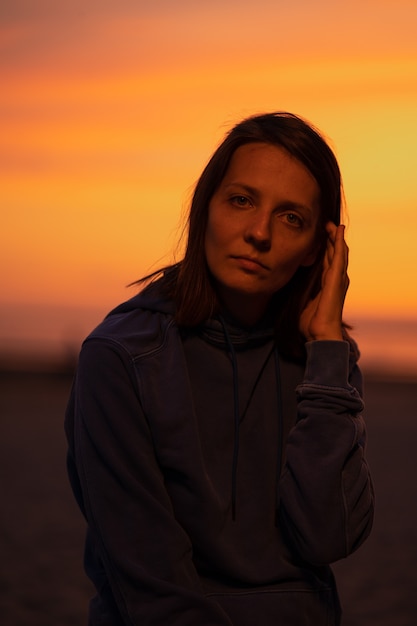 A european woman illuminated by neon light in a hat against the background of the sunset sky