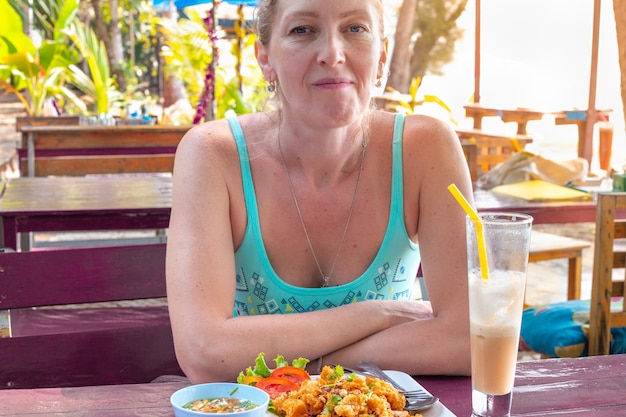 European woman in a thai cafe smiling on the table is a dish with spicy salad and a banana shake