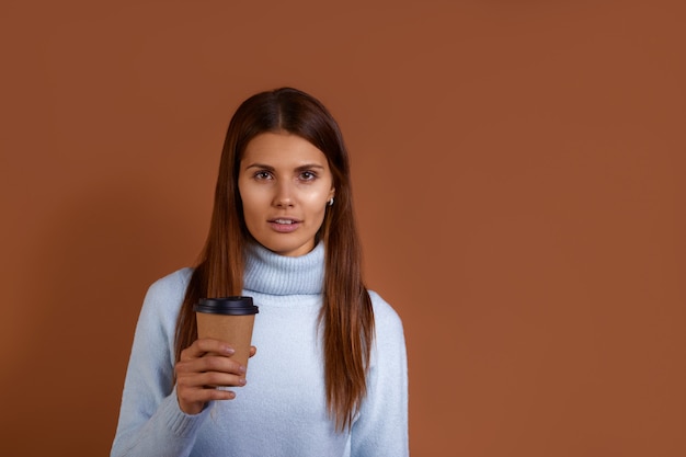 European woman wearing light blue sweater holds paper cup of coffee