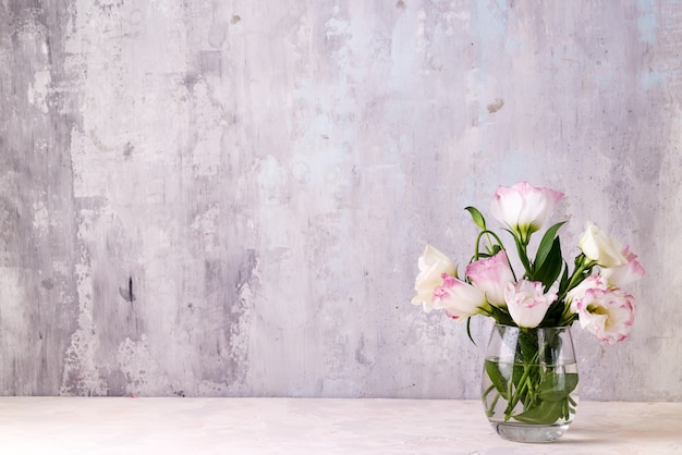 Eustoma flowers in vase on table near stone wall, space for text. Blank for postcards