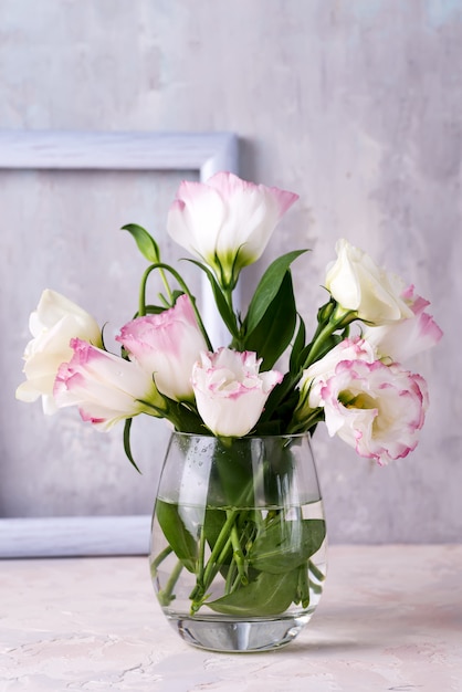 Eustoma flowers in vase on table near stone wall, space for text. Blank for postcards