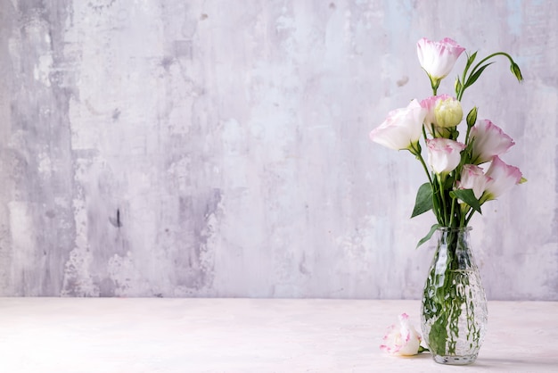 Eustoma flowers in vase on table near stone wall, space for text.