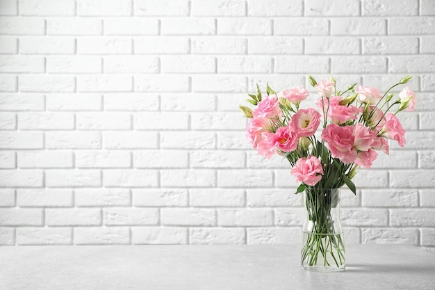 Eustoma flowers in vase on table near white brick wall space for text