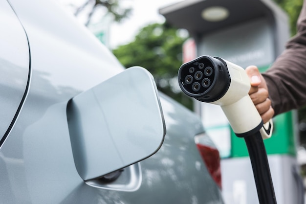 Ev car Electric car charging on parking lot. Male hand holding power cable supply plugged at Electric car charging station. Eco-friendly alternative energy. Future technology battery vehicle.