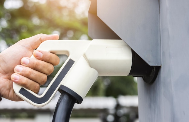 Ev car Electric car charging on parking lot. Male hand holding power cable supply plugged at Electric car charging station. Eco-friendly alternative energy. Future technology battery vehicle.