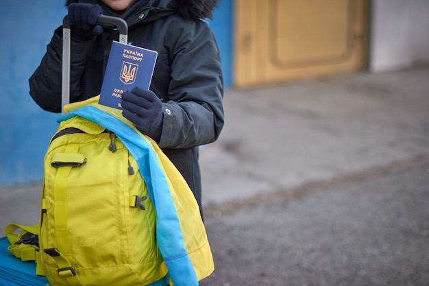 Evacuation of civilians sad child with the flag of Ukraine Refugee family from Ukraine crossing the border Hand holding a passport above the luggage with yellowblue flag Stop war support Ukraine