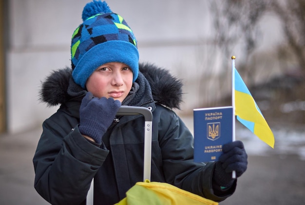 Evacuation of civilians sad child with the flag of Ukraine Refugee family from Ukraine crossing the border Hand holding a passport above the luggage with yellowblue flag Stop war support Ukraine