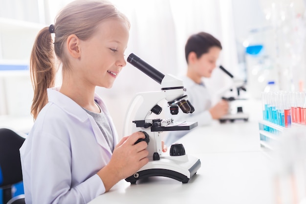 Even closer. Nice smart busy girl learning while using microscope and wearing lab coat