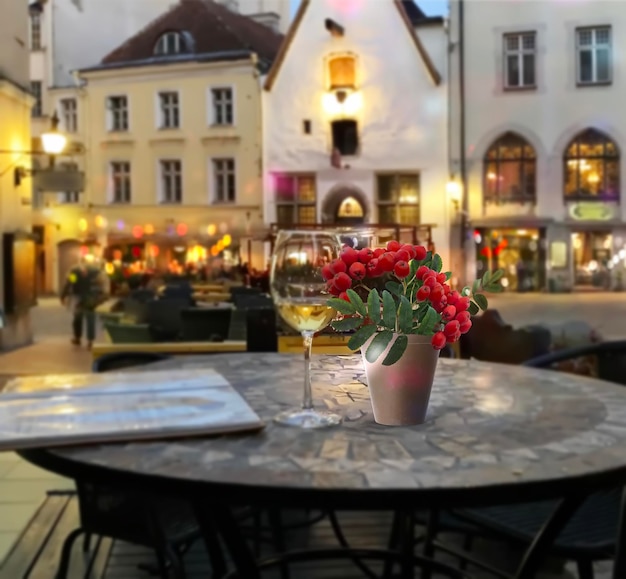 Evening street cafe glass of wine and red  rowan berry branch on table ,  people walk in Tallinn