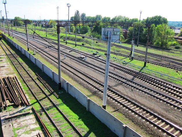 Evenly laid railroad rails crossing the frame diagonally Railroad track viewing platforms rails for repairs behind the fence Wires next to greenery Transfer switches traffic lights and mechanis