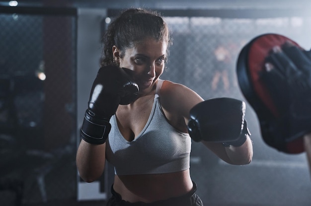 Every punch pays off Shot of a young woman practicing with her coach at a boxing gym