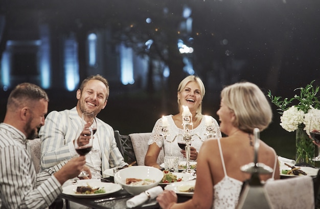 Everyone is laughing now. Successful joke. A group of adult friends have a rest and conversation in the backyard of the restaurant at evening time.