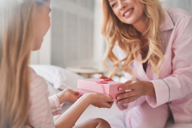 Everything for her princes. Young attractive mother giving a present to her cute little daughter while sitting on the bed at home