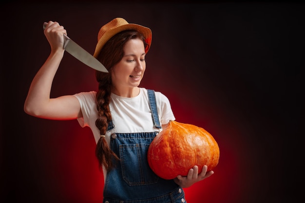 Evil farmer woman on a black and red background carves a lantern out of a ripe pumpkin with aknife