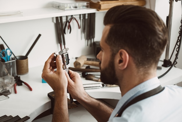 Exact size. Close up photo of a young male jeweler measuring ring with a tool in workshop. Jewelry manufacturing concept. Jewelry making workshop. Master's hands