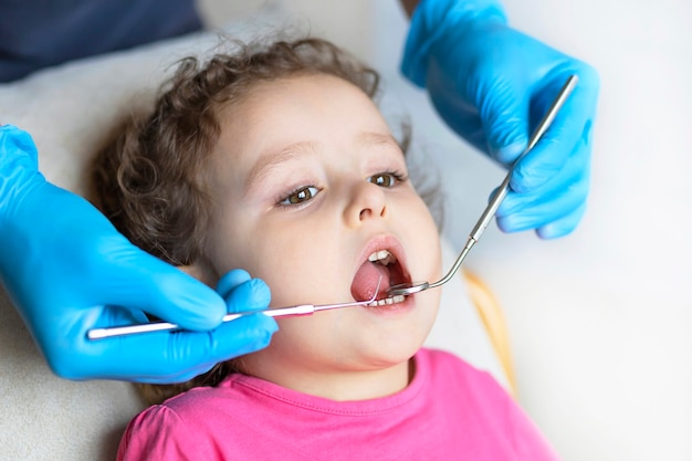 Examination, treatment teeth children. medical checkup oral cavity with instruments. dental hands, child in office. Cute girl smiling stomatology. kid in dentist chair.