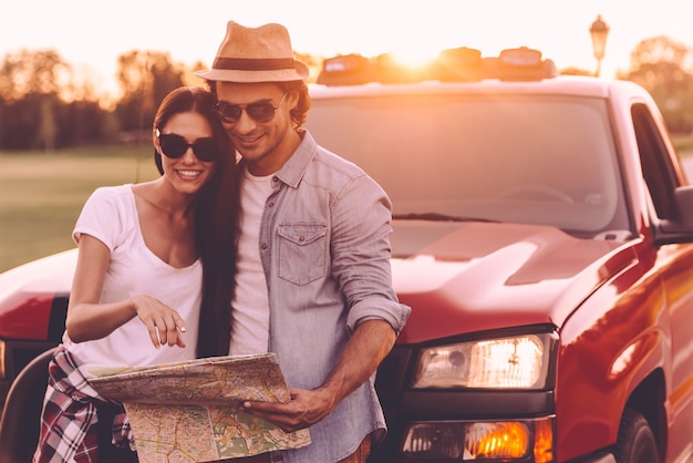 Examining map together. Beautiful young couple bonding to each other and leaning at their pick-up truck while examining map together