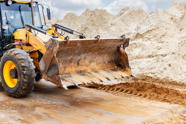 The excavator backfills the pit with the front bucket Moves soil around the construction site Closeup Heavy construction equipment