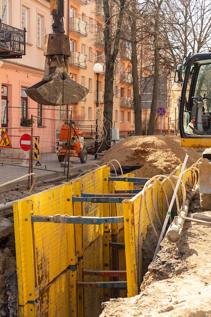 Excavator filling deep excavation supported by trench box with pipe bedding pea gravel during installation of drainage pipe