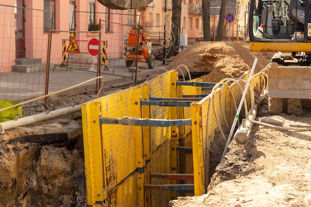 Excavator filling deep excavation supported by trench box with pipe bedding pea gravel during installation of drainage pipe