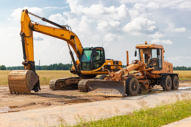 Photo the excavator and the grader stand side by side against the blue sky. heavy construction earthmoving equipment. construction of roads and underground communications. construction industry.