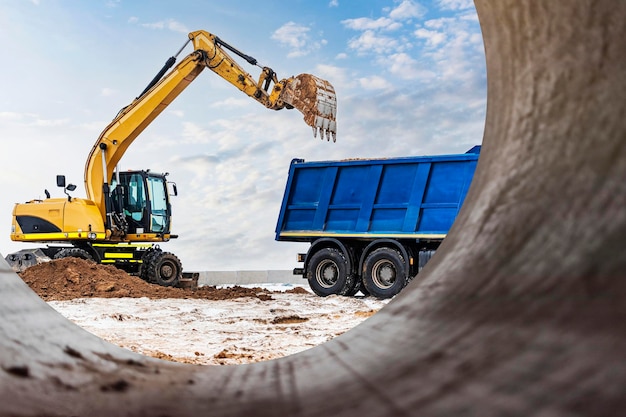 Photo an excavator loads soil or sand into a dump truck pit development earthworks with the help of heavy construction equipment