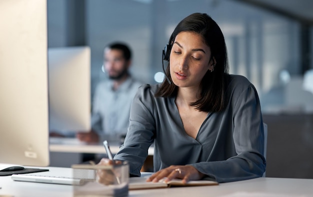 Excellent customer care around the clock Shot of a young woman using a headset and computer late at night in a modern office