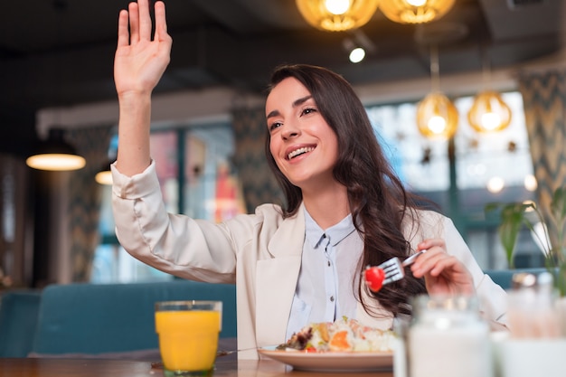 Excellent service. Beautiful merry energetic woman rising hand while eating lunch and smiling