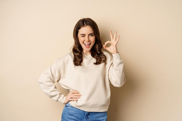 Excellent. Smiling beautiful woman showing okay, ok zero sign, approve smth good, praising and complimenting, beige background