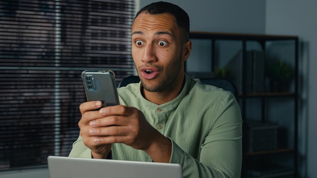 Excited african american businessman receiving email reading good news on mobile phone overjoyed man