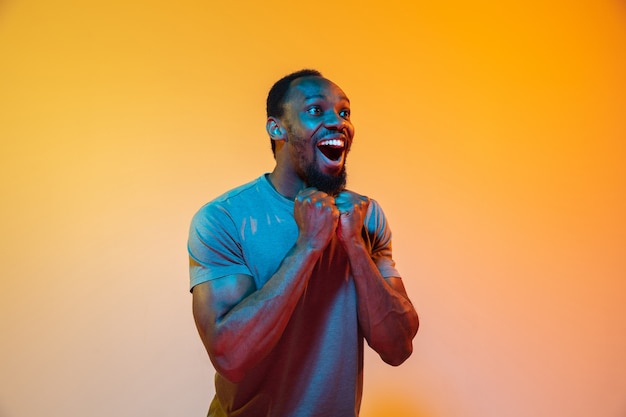 Excited. African-american man's modern portrait isolated on gradient orange studio background in neon light. Beautiful afro model. Concept of human emotions, facial expression, sales, ad. Copyspace.