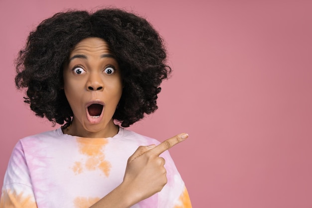 Excited African American woman looking at camera pointing finger on copy space Shopping sale