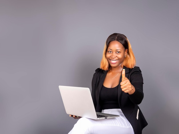 Excited african American young woman holding newest laptop and showing thumb up isolated over a Gray studio background